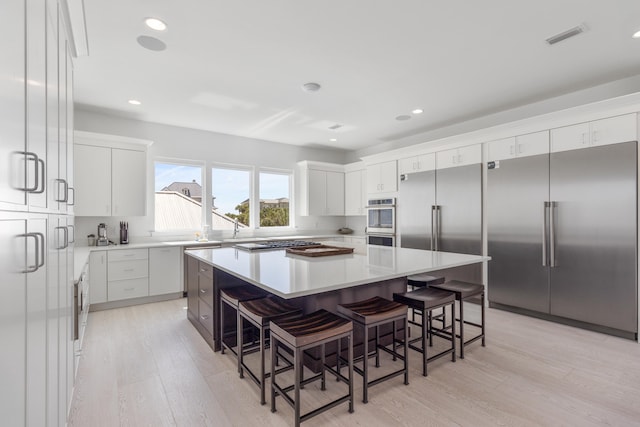 kitchen featuring a kitchen bar, stainless steel appliances, white cabinets, a center island, and light wood-type flooring