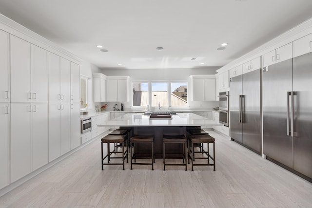 kitchen with appliances with stainless steel finishes, a kitchen island, white cabinets, light hardwood / wood-style floors, and a kitchen breakfast bar