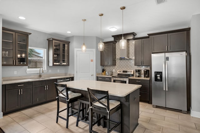 kitchen with a center island, wall chimney exhaust hood, a kitchen bar, decorative light fixtures, and stainless steel appliances