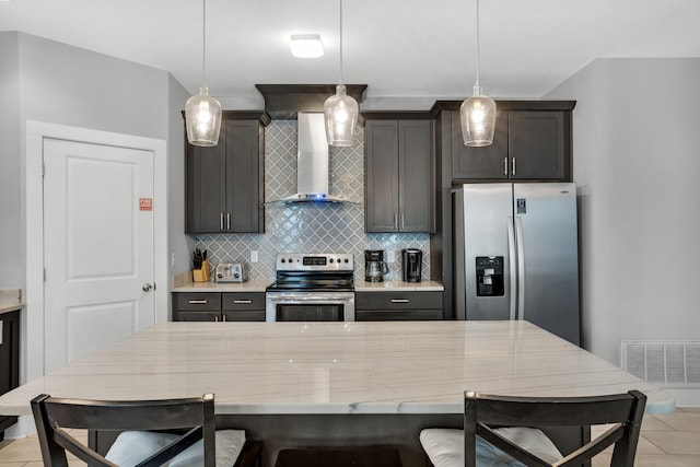 kitchen with light tile flooring, wall chimney range hood, stainless steel appliances, and pendant lighting