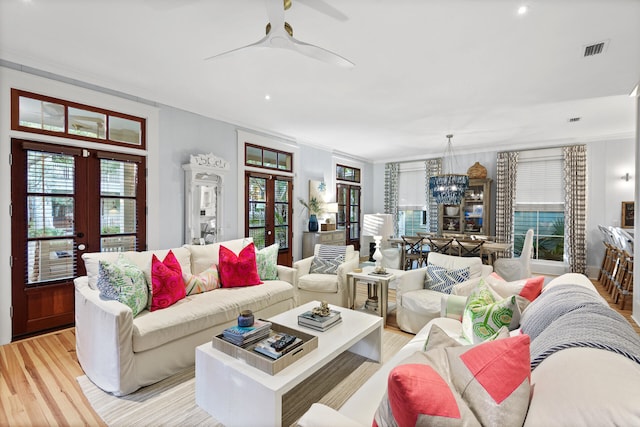 living room featuring ceiling fan with notable chandelier, french doors, light hardwood / wood-style floors, and crown molding