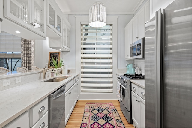 kitchen featuring white cabinets, light stone countertops, crown molding, appliances with stainless steel finishes, and light hardwood / wood-style floors