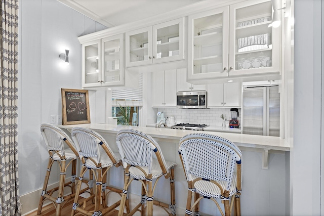 kitchen featuring white cabinets, a kitchen breakfast bar, stainless steel appliances, and backsplash