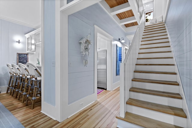 stairs with beamed ceiling and light wood-type flooring