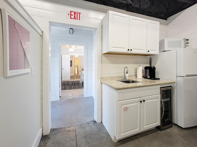 kitchen with white appliances, concrete flooring, wine cooler, white cabinets, and sink