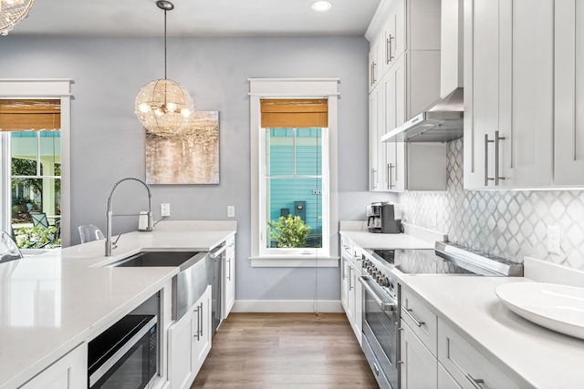 kitchen featuring a healthy amount of sunlight, stainless steel appliances, white cabinets, and wall chimney range hood