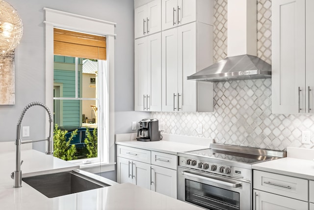 kitchen with decorative light fixtures, white cabinetry, sink, wall chimney range hood, and stainless steel range