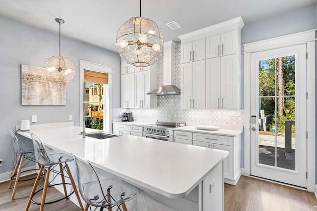 kitchen with a kitchen bar, high end stainless steel range oven, wall chimney range hood, and a chandelier