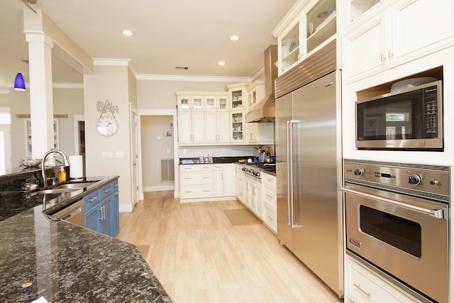 kitchen featuring sink, crown molding, light hardwood / wood-style flooring, dark stone countertops, and built in appliances