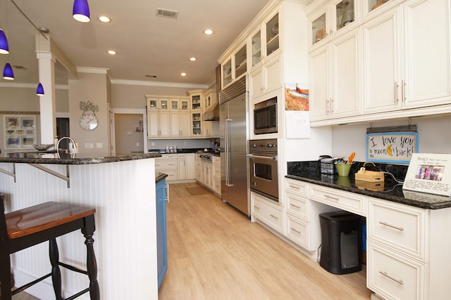 kitchen with built in appliances, a breakfast bar, light wood-type flooring, crown molding, and dark stone countertops