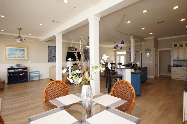 dining area featuring decorative columns, light wood-type flooring, crown molding, sink, and ceiling fan