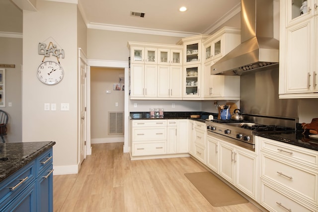 kitchen with stainless steel gas cooktop, ornamental molding, wall chimney range hood, dark stone counters, and light hardwood / wood-style floors