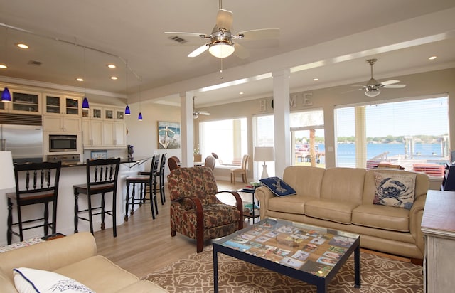 living room featuring crown molding, light wood-type flooring, ceiling fan, and a water view