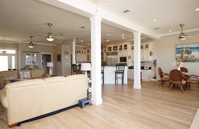 living room featuring ornamental molding, ceiling fan, light hardwood / wood-style floors, and decorative columns