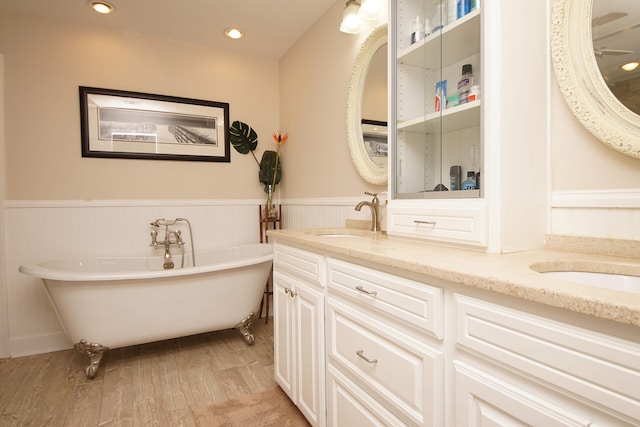 bathroom with wood-type flooring, vanity with extensive cabinet space, double sink, and a bath to relax in