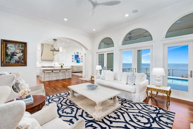 living room featuring a water view, ornamental molding, ceiling fan with notable chandelier, and hardwood / wood-style flooring