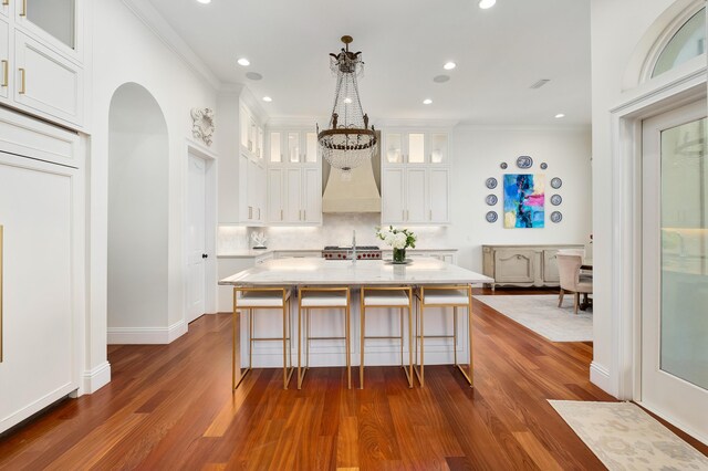 kitchen featuring a kitchen island, dark hardwood / wood-style flooring, a kitchen bar, ornamental molding, and white cabinets