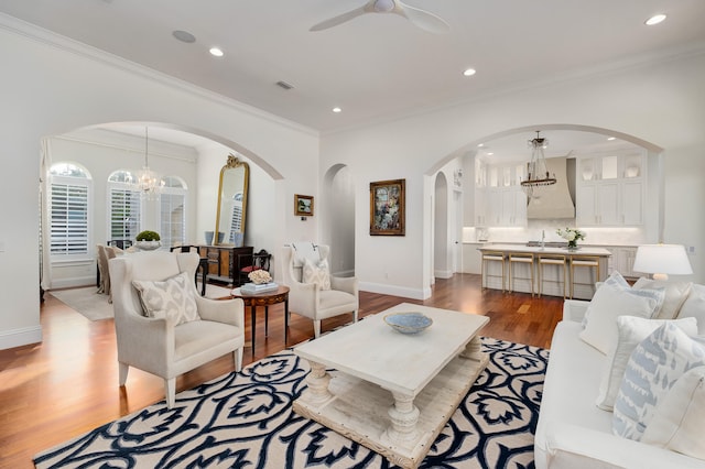 living room with ceiling fan with notable chandelier, light hardwood / wood-style floors, crown molding, and sink