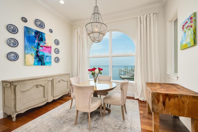 dining area with a water view, dark hardwood / wood-style floors, an inviting chandelier, and crown molding