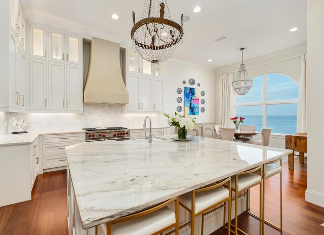 kitchen featuring white cabinetry, stainless steel range, an island with sink, and custom exhaust hood