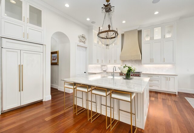 kitchen with a center island with sink, a breakfast bar, custom range hood, and wood-type flooring