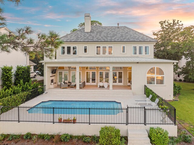 back house at dusk featuring outdoor lounge area, a fenced in pool, a patio area, and french doors