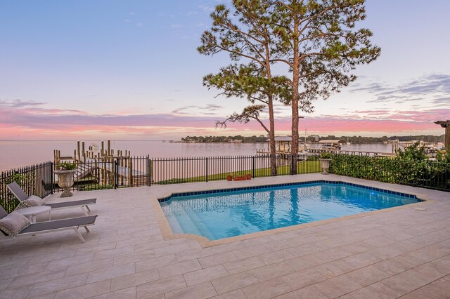 pool at dusk featuring a water view and a patio area