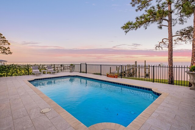 pool at dusk with a water view and a patio