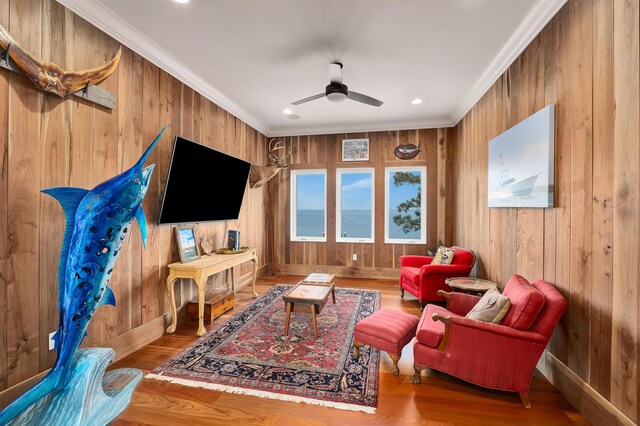 living room featuring ornamental molding, hardwood / wood-style flooring, ceiling fan, and wooden walls