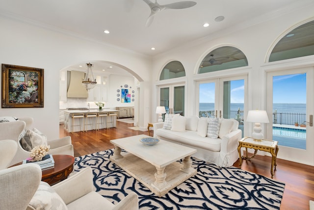 living room with a water view, ceiling fan with notable chandelier, light hardwood / wood-style floors, and ornamental molding