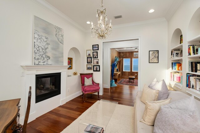 living room featuring built in shelves, dark wood-type flooring, ornamental molding, and a notable chandelier