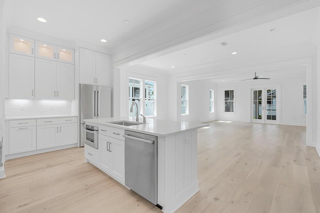 kitchen featuring light wood finished floors, white cabinets, appliances with stainless steel finishes, light countertops, and a sink