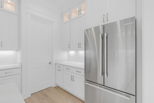 kitchen featuring light wood finished floors, high quality fridge, white cabinets, and backsplash