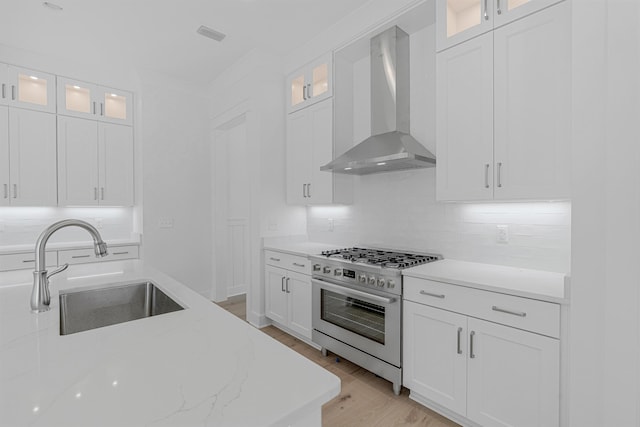 kitchen with tasteful backsplash, wall chimney range hood, white cabinetry, a sink, and gas stove