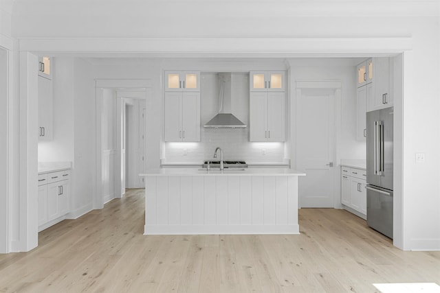 kitchen with high end fridge, light countertops, light wood-style flooring, and wall chimney exhaust hood