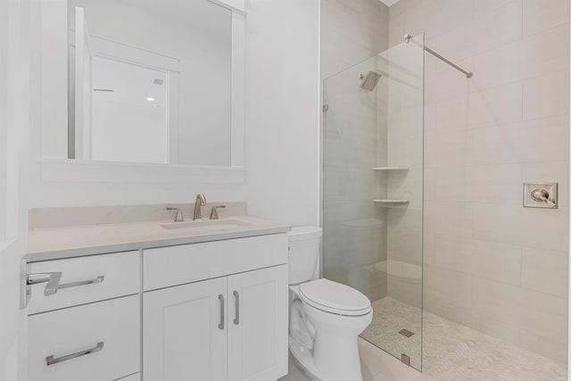 full bathroom featuring toilet, tiled shower, and vanity