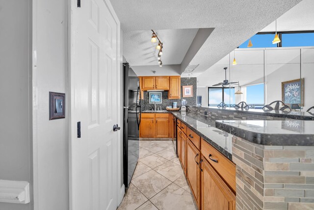 kitchen with a textured ceiling, sink, tasteful backsplash, black refrigerator, and track lighting