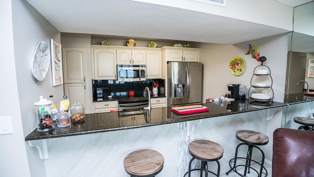 kitchen with kitchen peninsula, dark stone countertops, stainless steel appliances, and a kitchen bar