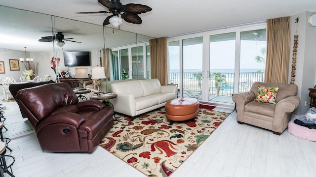 living room featuring light wood-type flooring, ceiling fan with notable chandelier, and a water view