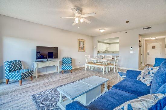 living room featuring ceiling fan, a textured ceiling, and light wood-type flooring