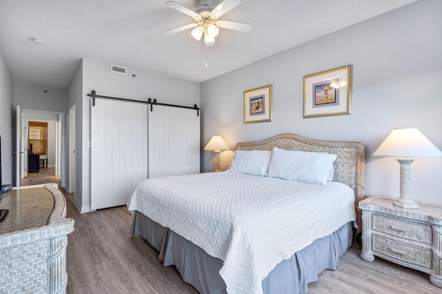 bedroom with light hardwood / wood-style flooring, ceiling fan, and a barn door