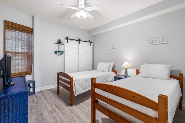 bedroom featuring ceiling fan, light wood-type flooring, and a barn door