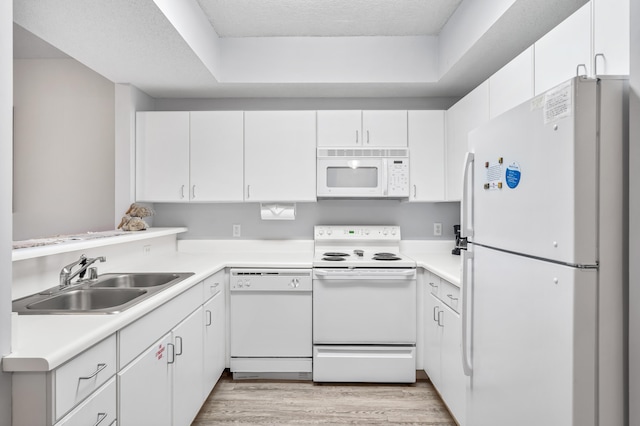 kitchen featuring sink, white appliances, light wood-type flooring, white cabinetry, and a tray ceiling