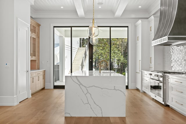 kitchen featuring high end range, light hardwood / wood-style floors, decorative light fixtures, a center island with sink, and custom range hood