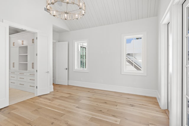 unfurnished bedroom featuring lofted ceiling, light wood-type flooring, and an inviting chandelier