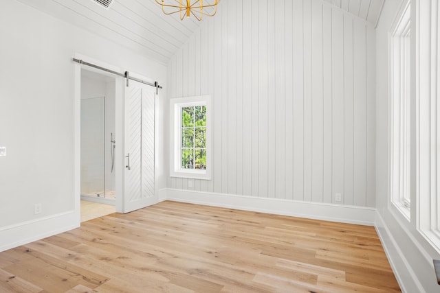 unfurnished room featuring light hardwood / wood-style flooring, lofted ceiling, and a barn door