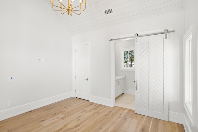 unfurnished bedroom with connected bathroom, light hardwood / wood-style flooring, lofted ceiling, and a barn door