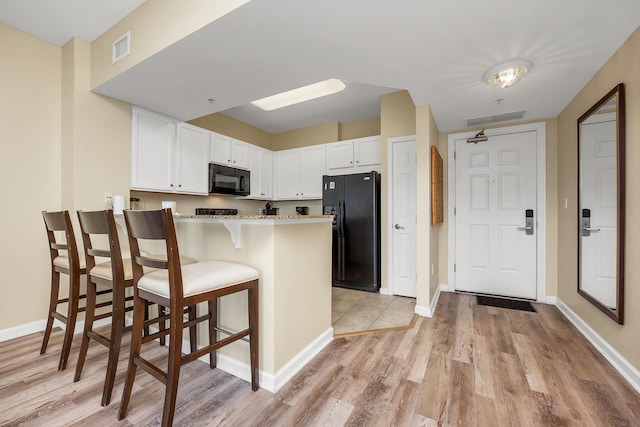 kitchen with kitchen peninsula, white cabinetry, a kitchen breakfast bar, and black appliances