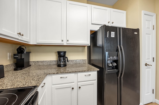 kitchen with stone countertops, white cabinetry, and black fridge