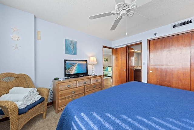 bedroom with a textured ceiling, ceiling fan, light carpet, and ensuite bathroom